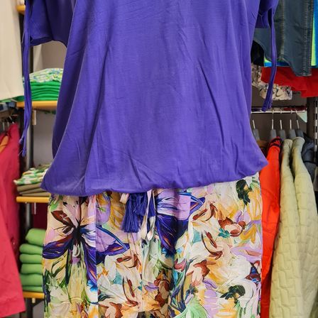 Ein lila Bluse mit Blumenmuster wird in einem Bekleidungsgeschäft ausgestellt, mit anderen Artikeln im Hintergrund.