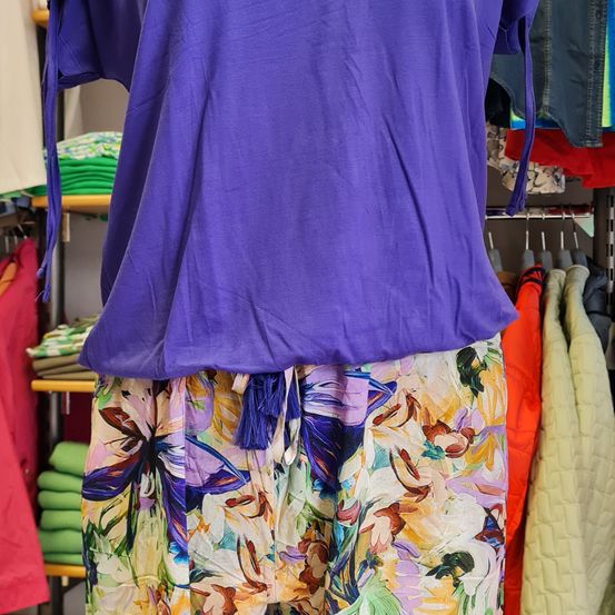 Ein lila Bluse mit Blumenmuster wird in einem Bekleidungsgeschäft ausgestellt, mit anderen Artikeln im Hintergrund.