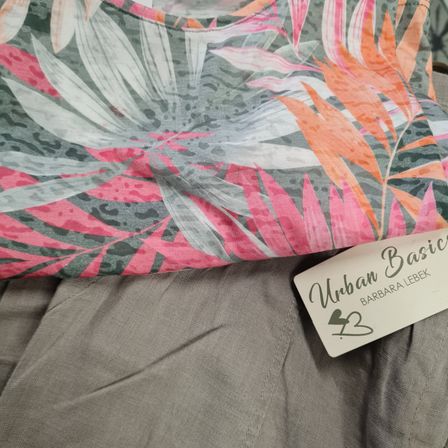 Ein rosa und graues Blumenmuster-Stoff mit Leopardenmuster ist über einem grauen Stoff gefaltet. Ein weißer Aufkleber mit 'Urban Basics' und 'BARBARA LEBEK' ist sichtbar.