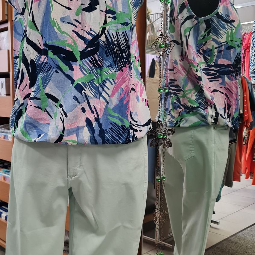Zwei Mannequins präsentieren Mode-Oberteile mit abstrakten Blumendrucken in Blau, Rosa und Grün. Beide sind mit mintgrünen Hosen kombiniert.
