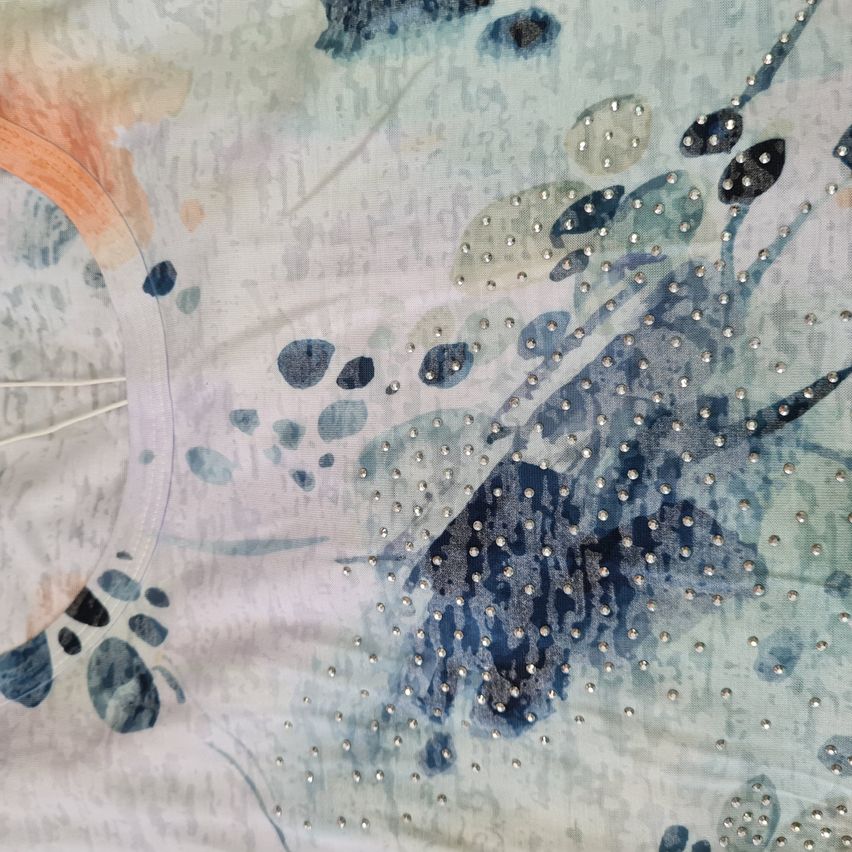 Ein abstraktes Design auf weißem Stoff zeigt blaue und orange Wasserfarbenspritzer mit verstreuten silbernen Perlen. Das Design ist detailreich und filigran.