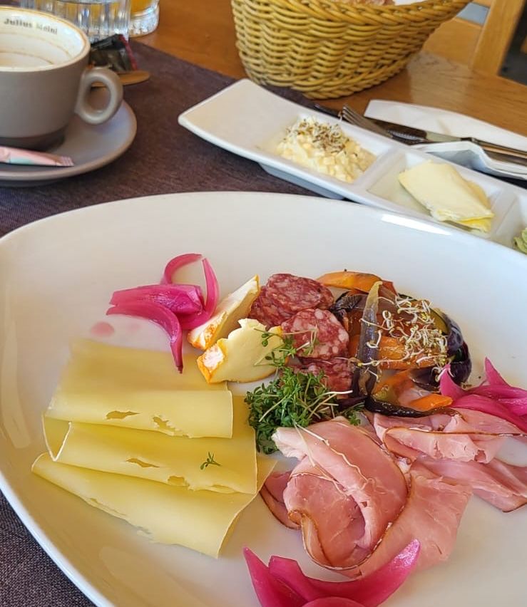 Ein Teller mit verschiedenen Käsesorten, Wurstwaren und Gemüsen mit einer Tasse Kaffee auf einem Untertasse.