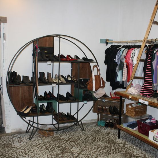 Ein Boutique-Laden mit einem kreisförmigen Schuhregal und einem Kleiderständer. Das Schuhregal ist mit verschiedenen Schuhen gefüllt, und der Kleiderständer hat eine Vielzahl von Kleidungsstücken.