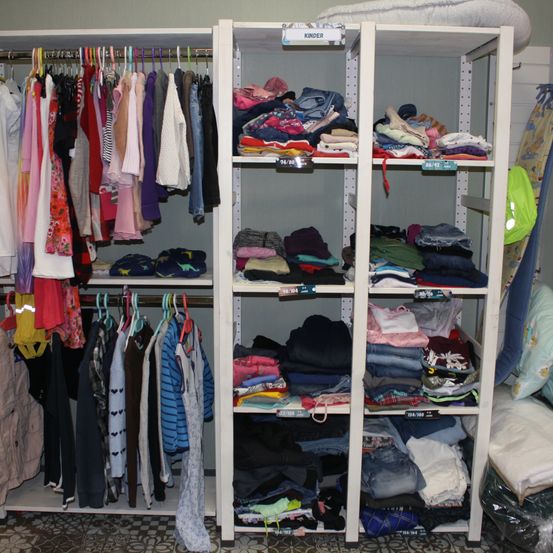 Ein gut organisierter Kleiderschrank mit ordentlich gefalteter Kleidung auf Regalen und an Kleiderbügeln, beschriftet mit 'Kinder'.
