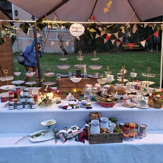 Ein festlicher Marktstand im Freien mit einer Vielzahl von Dekorationsartikeln, Kerzen und Gläsern unter einem Baldachin. Eine Person in einer blauen Jacke geht in der Nähe vorbei.