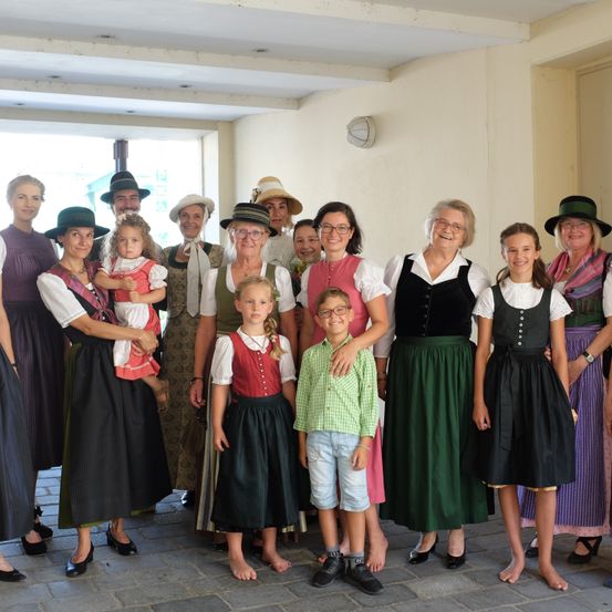 Eine Gruppe von Frauen und Kindern in traditioneller Kleidung, einschließlich Dirndl und Schürzen, posiert für ein Foto.