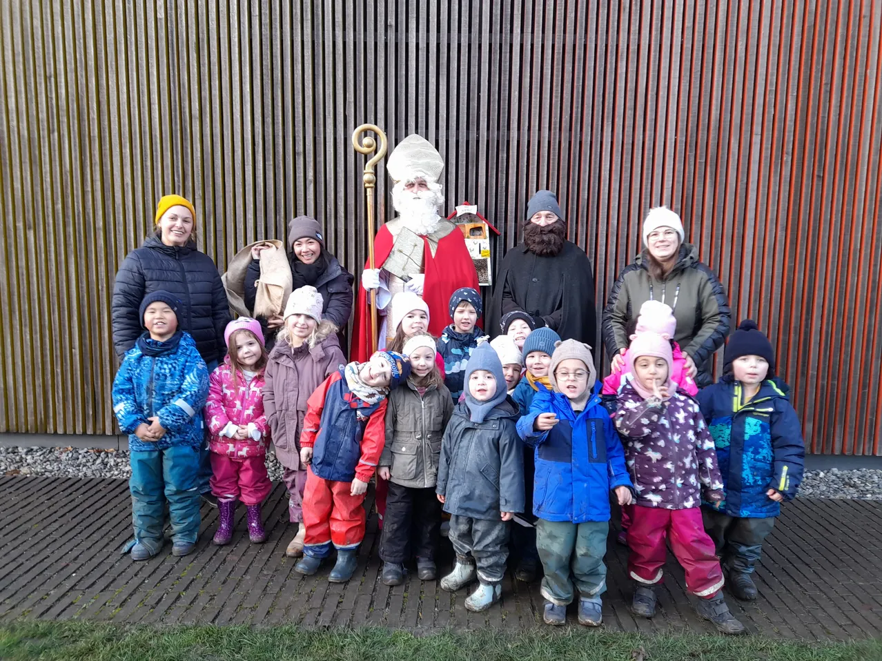Eine Gruppe von Kindern und Erwachsenen steht für ein Foto mit dem Weihnachtsmann vor einem Gebäude.
