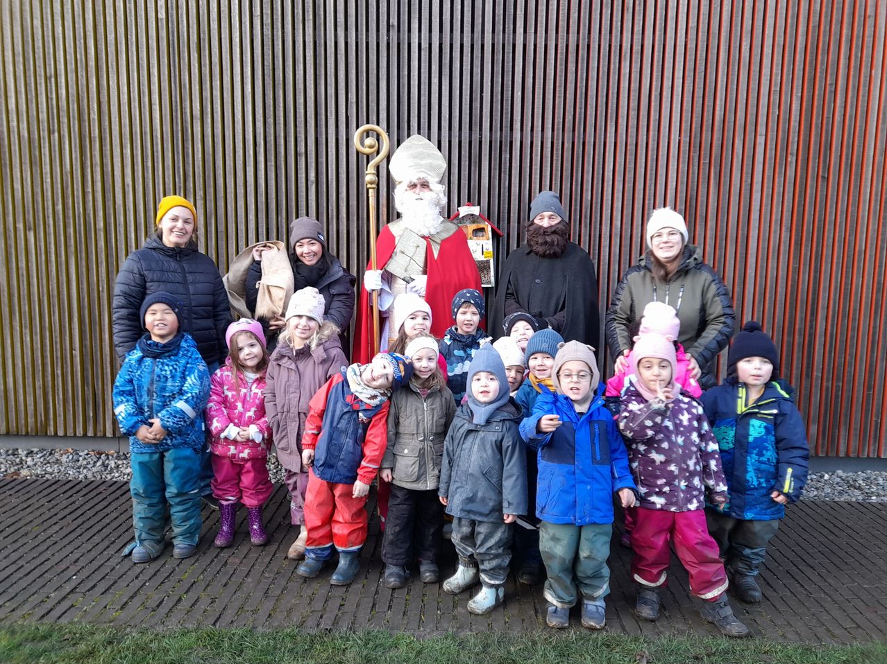 Eine Gruppe von Kindern und Erwachsenen steht für ein Foto mit dem Weihnachtsmann vor einem Gebäude.