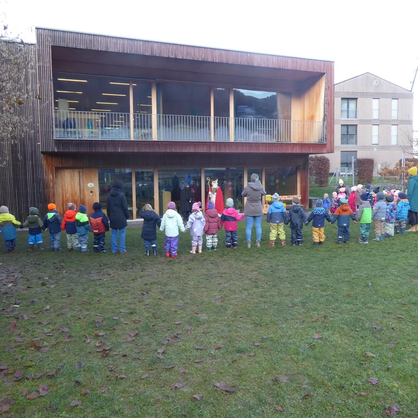 Eine Gruppe von Kindern in Winterkleidung steht in einer Reihe vor einem modernen Gebäude.