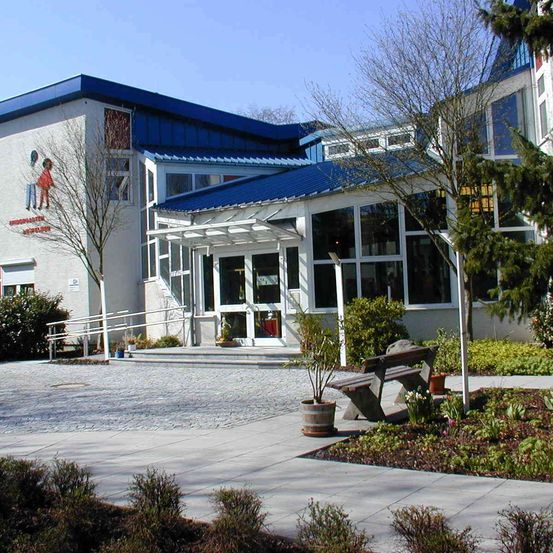 Ein weißes Gebäude mit blauem Dach hat eine Wandmalerei, große Fenster und eine Bank davor.