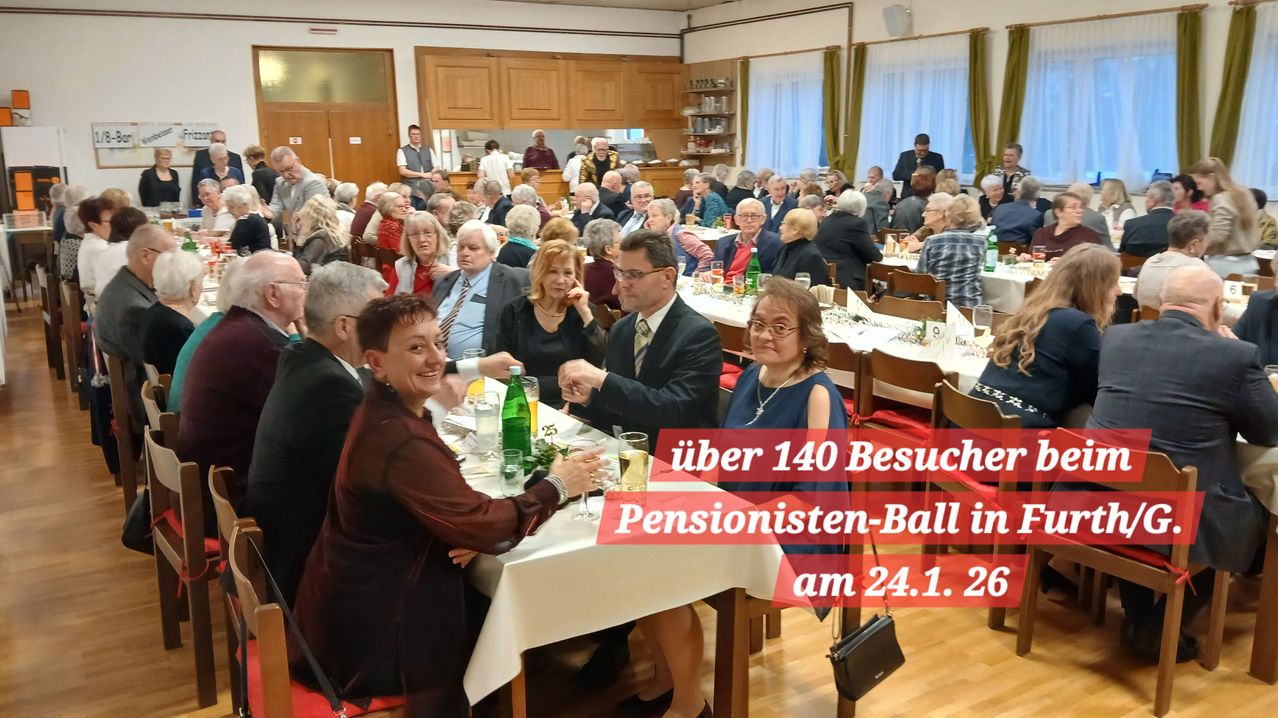 Eine große Gruppe älterer Menschen sitzt in einem Speisesaal an Tischen und feiert ein Ereignis. Flaschen und Gläser stehen auf den Tischen, und eine Frau lächelt.