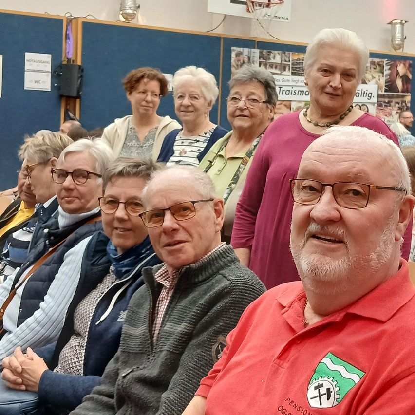 Eine Gruppe älterer Menschen mit Brillen sitzt in einem Raum. Sie lächeln und scheinen für ein Foto zu posieren.