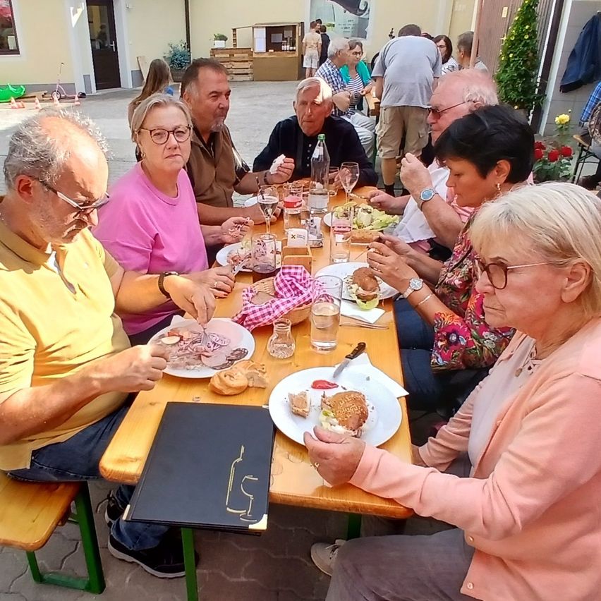 Eine Gruppe von Menschen sitzt um einen Tisch in einem Restaurant im Freien und genießt ihre Mahlzeiten und Getränke.