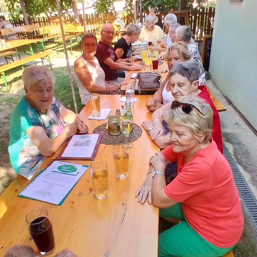 Eine Gruppe älterer Frauen sitzt an einem Tisch in einem Restaurant im Freien, einige mit Biergläsern, andere mit Menüs.