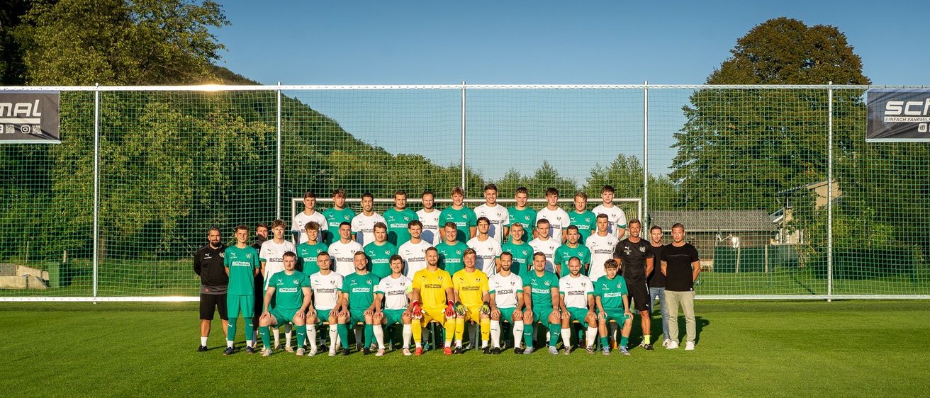 Eine Fußballmannschaft in grünen und weißen Trikots posiert für ein Mannschaftsfoto auf einem Feld mit einem Netz im Hintergrund.