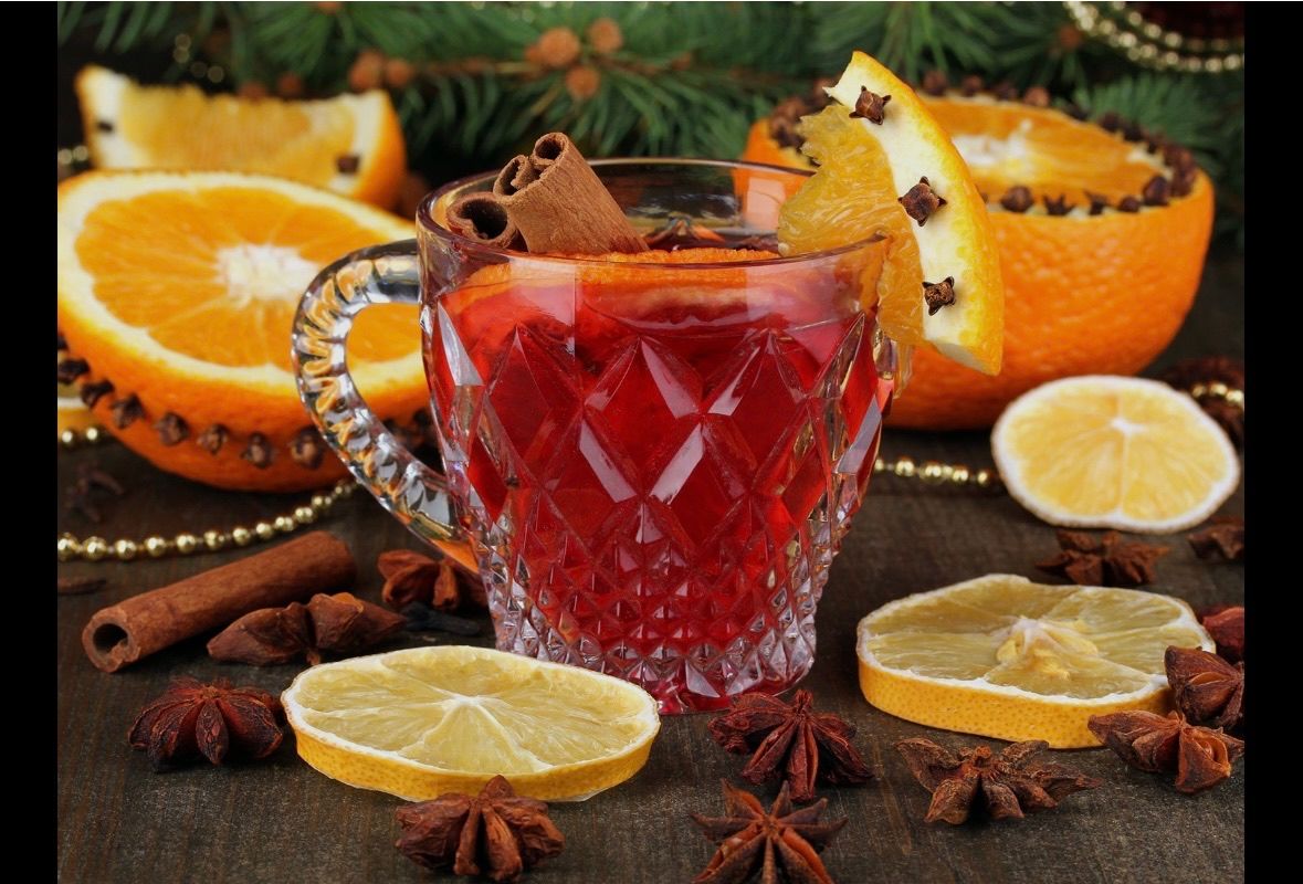 Ein festlicher roter Drink in einem Glas mit einer Zimtstange und Orangenscheibe, umgeben von Zitrusscheiben, Sternanis und Perlen.
