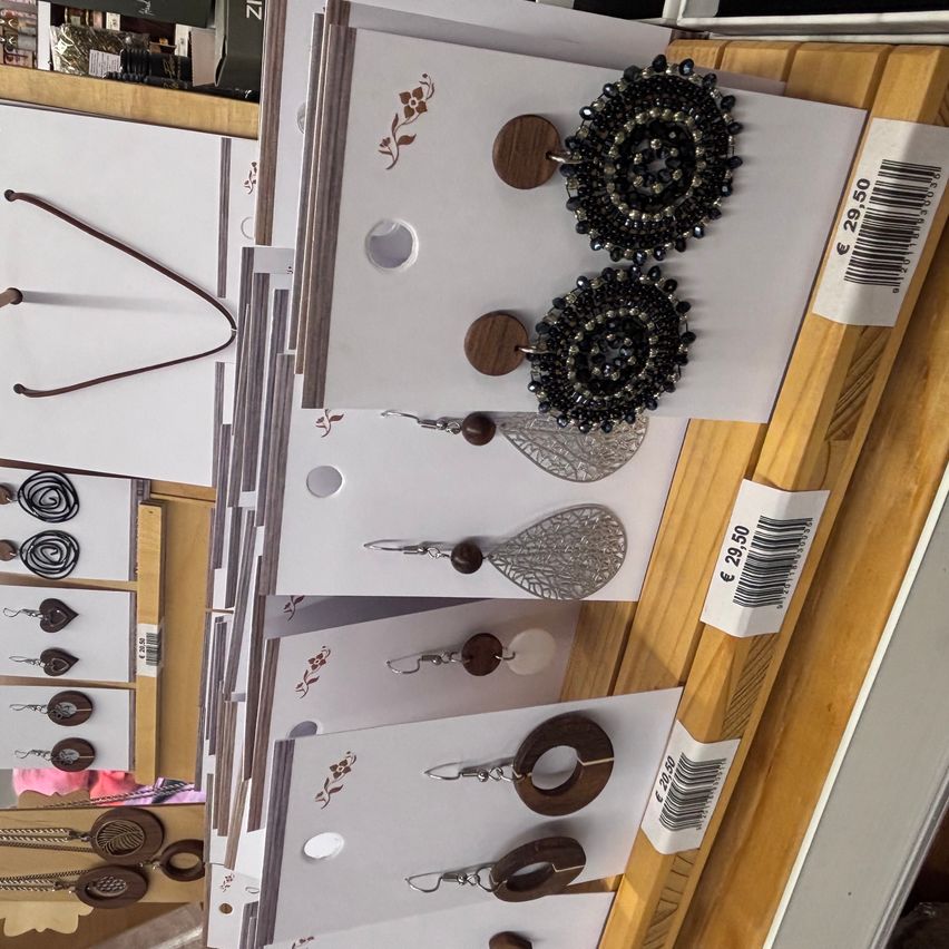 Eine Ausstellung verschiedener Schmuckstücke auf einem Holzständer, darunter Ohrringe mit Perlen und Holzakzenten, herzförmige Anhänger und verschiedene Halsketten. Jedes Stück ist einzeln verpackt.