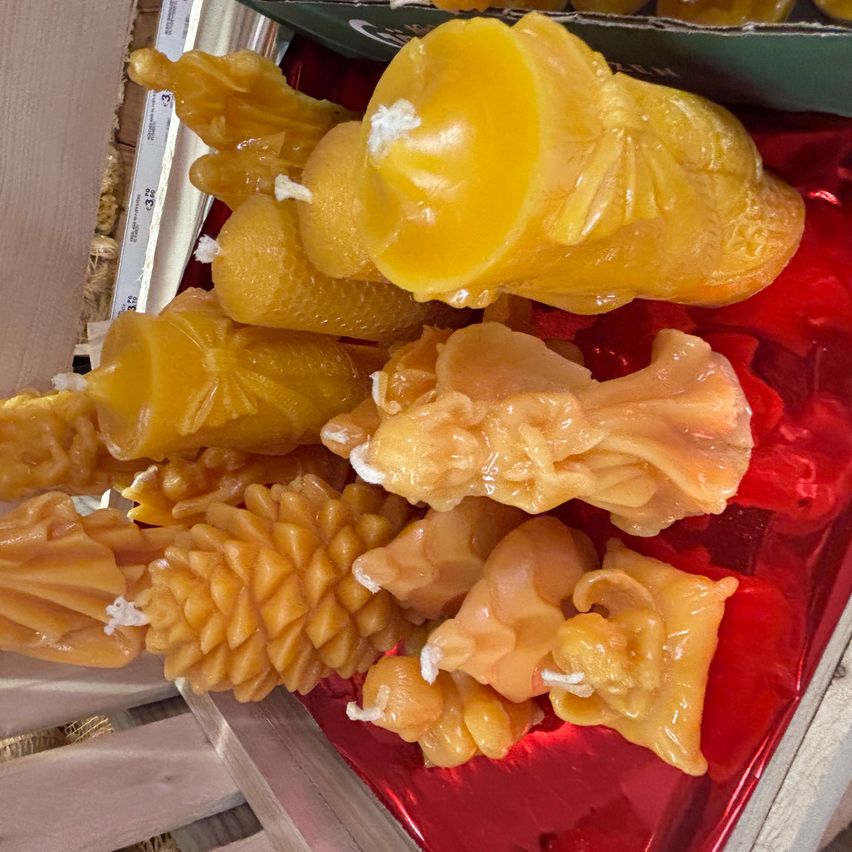 Eine Sammlung gelber Kerzen in verschiedenen Formen, einschließlich menschlicher Figuren, Kegel und anderer, auf einer roten Oberfläche präsentiert.