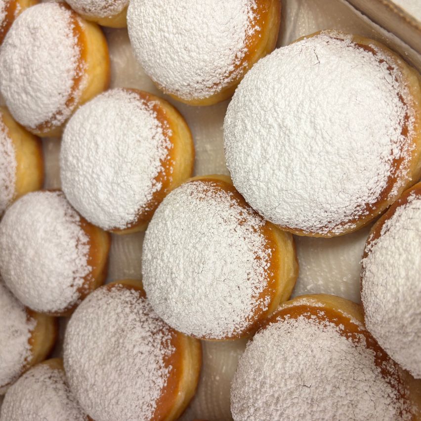 Eine Nahaufnahme von mehreren puderzuckerbedeckten Donuts, die in einer Schachtel angeordnet sind.