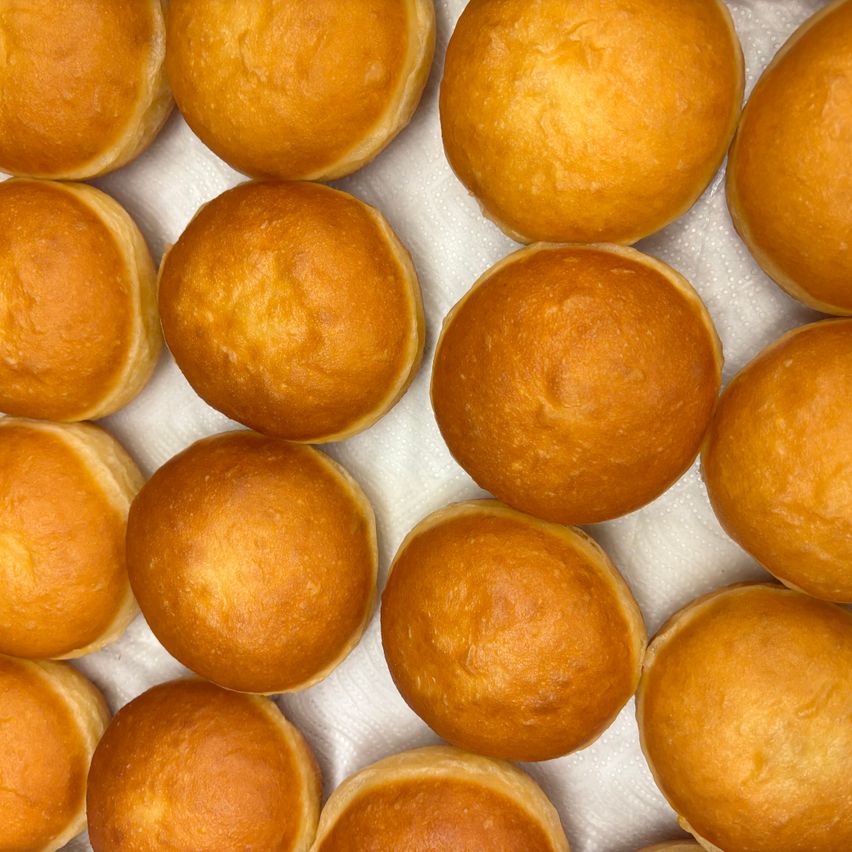 Ein Nahaufnahme einer Schale voller goldbrauner, fluffiger Brötchen, jedes mit einer leicht knusprigen Außenseite und einem weichen, luftigen Inneren. Die Brötchen sind in einer ordentlichen Reihe angeordnet und zeigen ihre perfekte Form und goldene Farbe.