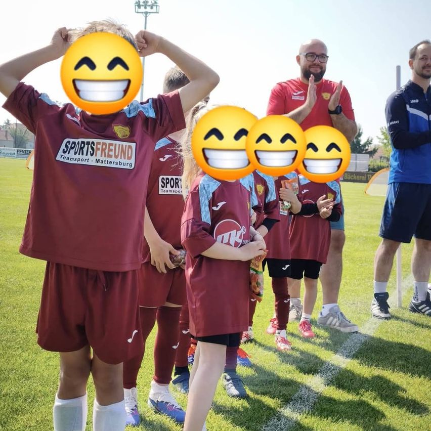 Eine Gruppe von Kindern in burgunderroten Trikots mit dem Text SportsFreund und Transport Mattersburg auf der Vorderseite, lächelnd und in einer Reihe auf einem Rasenfeld stehend.