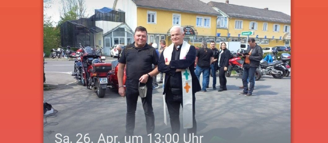 Zwei Männer stehen vor einem gelben Gebäude mit geparkten Motorrädern im Hintergrund. Der Mann auf der linken Seite hält einen Becher. Der Mann auf der rechten Seite hält ein weißes Tuch mit einem Kreuz. Das Bild hat einen Wasserzeichen mit dem Text 'Sa, 26. Apr. um 13:00 Uhr Motorradsegnung!'.