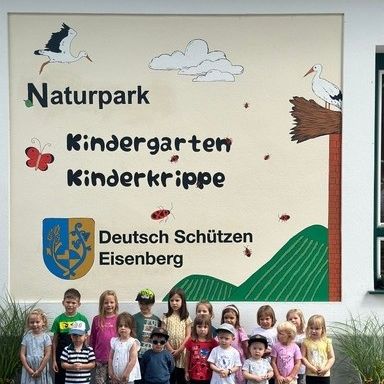 Eine Gruppe von Kindern posiert für ein Foto vor einer Wandmalerei im Naturpark Kindergarten Kinderkrippe.