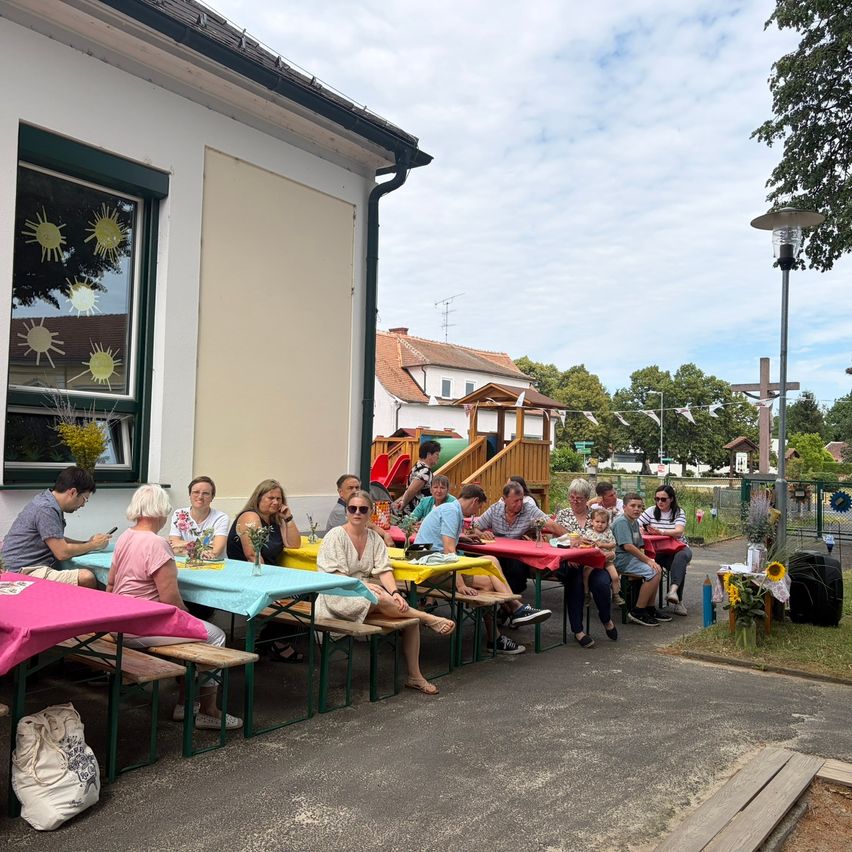 A group of people sitting at tables outside a building with a playground and trees in the background.