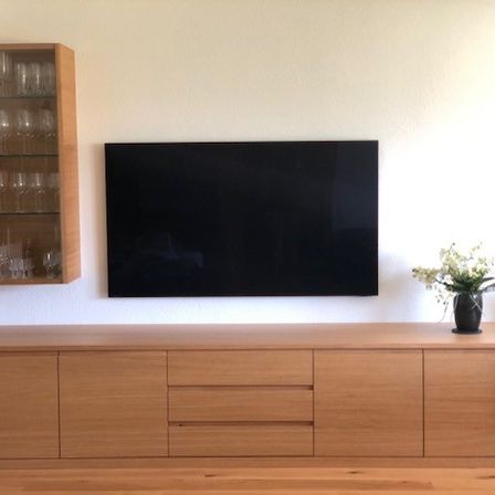 Ein Wohnzimmer mit einem hölzernen Entertainment-Schrank, einem montierten Flachbildfernseher, einem Weinglasschrank und einer Topfpflanze.