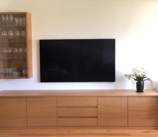 Ein Wohnzimmer mit einem hölzernen Entertainment-Schrank, einem montierten Flachbildfernseher, einem Weinglasschrank und einer Topfpflanze.