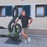 Ein Mann steht neben einer großen musikalischen Noten-Skulptur vor einem Gebäude mit einem Hirschlogo und dem Wort 'Wirtshaus'.