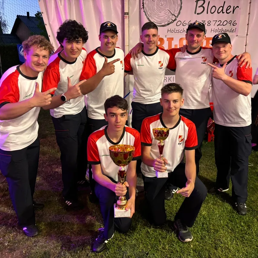 Eine Gruppe junger Männer in Sportuniformen posiert mit ihren Trophäen auf einem Rasenfeld unter einem Banner.