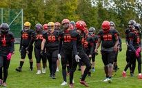 Eine Gruppe von Footballspielern in schwarzen Trikots, Helmen und Handschuhen läuft über ein Feld. Die Spieler sind in einer Reihe aufgestellt, möglicherweise in Vorbereitung auf ein Spiel.