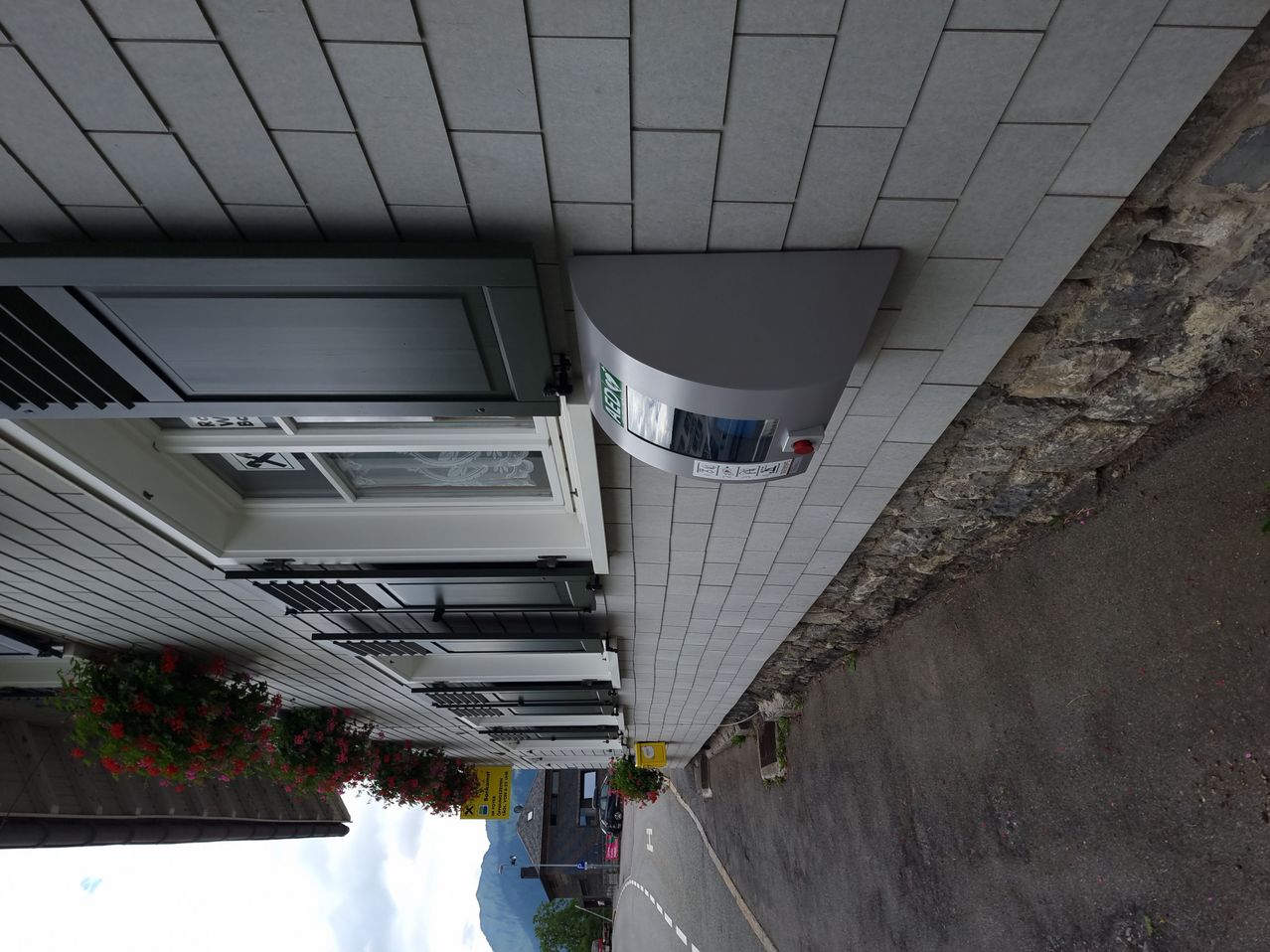 Ein graues Gebäudeaußen mit einer grauen Tür, einer grauen Metallbox mit einem roten Knopf und einer grauen gefliesten Wand.