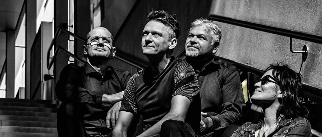 Vier Personen sitzen auf Betonstufen, in Freizeitkleidung gekleidet. Sie scheinen für ein Foto zu posieren.