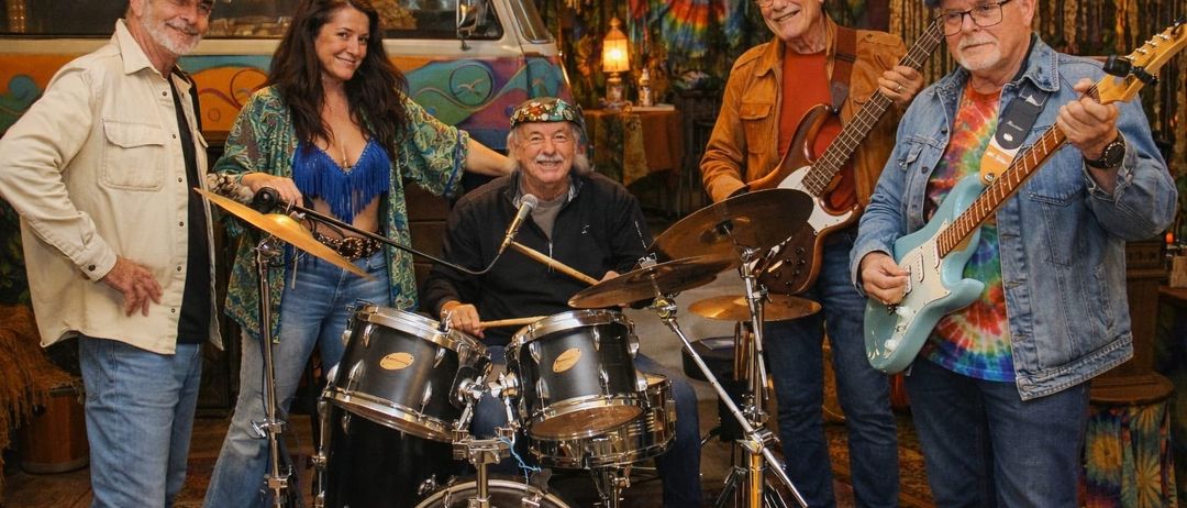 Fünf Musiker posieren für ein Foto. Eine Frau in einem grünen Kleid, ein Mann mit Hut und drei Männer mit Gitarren. Dahinter ein VW-Bus und ein bunter Hintergrund.