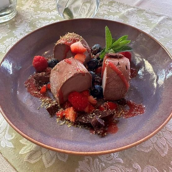 Ein Teller mit drei Stücken Schokoladenmousse, überzogen mit Beeren und Schokoladenraspeln, garniert mit Minzblättern.