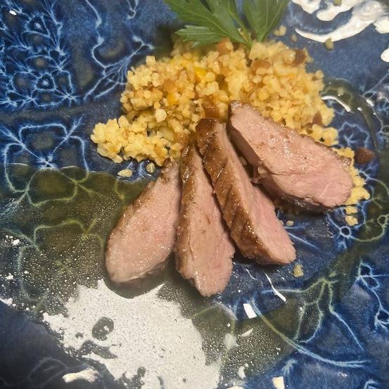 Ein Teller mit geschnittenem Entenbrust und einer Schicht goldenen Couscous, garniert mit einem Petersilienzweig.