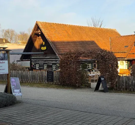 Ein traditionelles deutsches Gasthaus mit einem roten Dach und einem Schild, das 'Herberts Stuben' besagt. Das Gasthaus ist von einem Holzzaun umgeben und hat einen kleinen Garten.