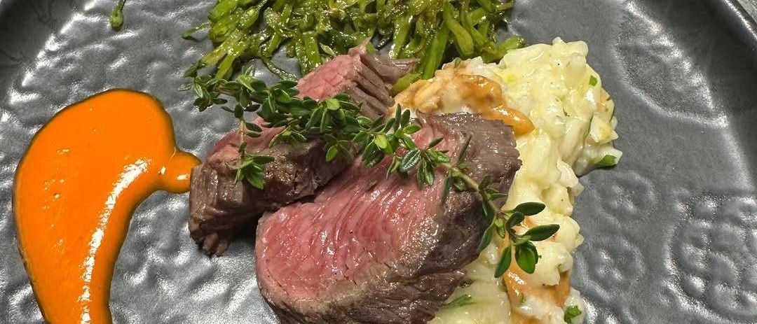 Ein Teller mit einem Stück Steak, Kartoffelpüree, grünen Bohnen und oranger Sauce.