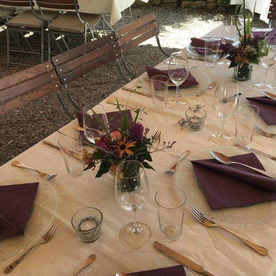 Ein Tisch für eine Mahlzeit gedeckt mit Weingläsern, Besteck und Blumen in einer Vase. Der Tisch ist mit einer weißen Tischdecke bedeckt.