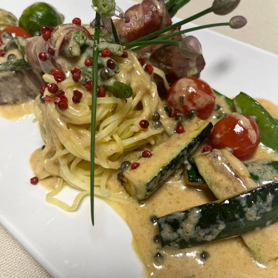 Ein Teller mit Nudeln in cremiger Sauce, garniert mit roten Paprika, Spargel und Kirschtomaten.
