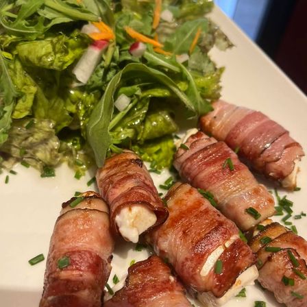Ein Teller mit baconumwickelten Fleischrollen und einer Beilage aus grünem Salat, garniert mit Schnittlauch.
