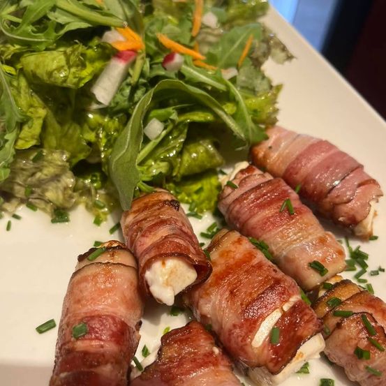 Ein Teller mit baconumwickelten Fleischrollen und einer Beilage aus grünem Salat, garniert mit Schnittlauch.