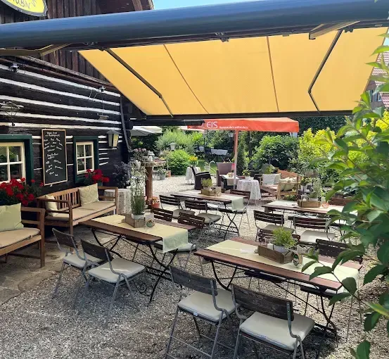 Ein Restaurant im Freien mit einer Holzbank, einem Tisch mit einem Topf und einem gelben Baldachin. Das Restaurant hat einen Garten mit Pflanzen und Blumen.