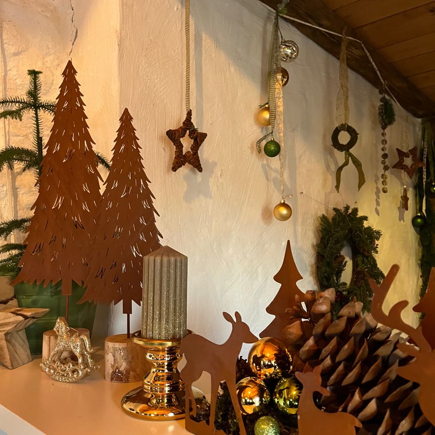 A shelf with various Christmas decorations including metal trees, a star, a candle, and pine cones. A deer and pinecones are on the right.