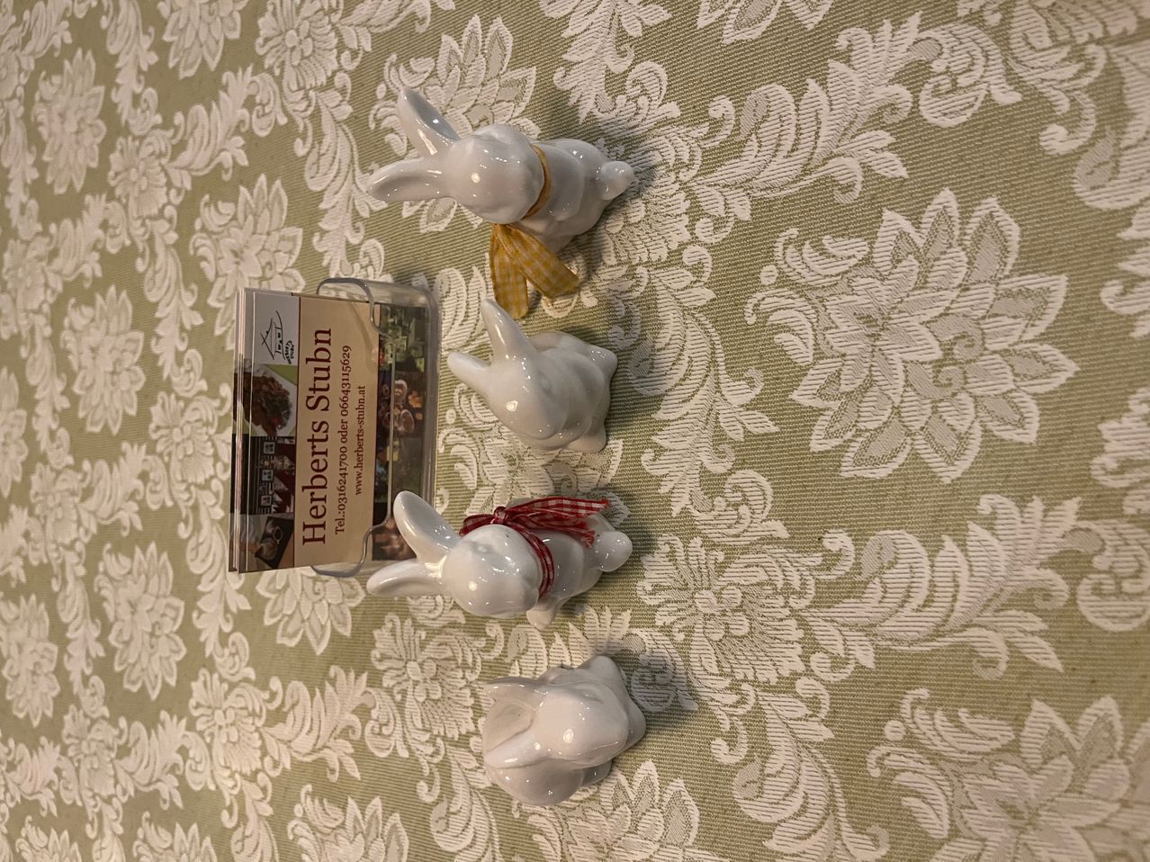 Vier Keramikhasen auf einer grün gemusterten Oberfläche. Drei haben Schleifen um den Hals und einer hat eine Karte neben sich platziert.