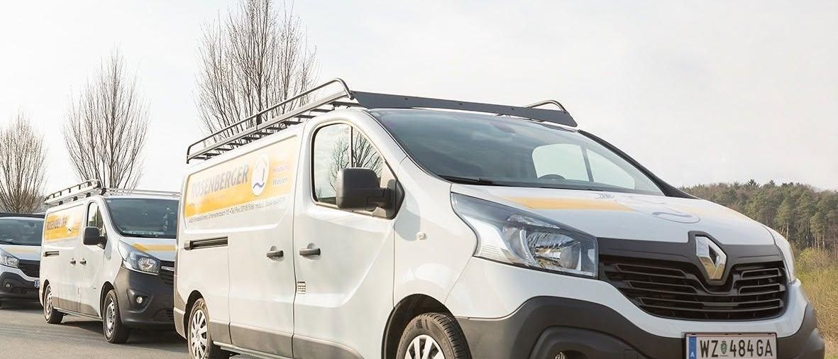 Eine Reihe weißer Lieferwagen mit gelben und schwarzen Markierungen ist am Straßenrand geparkt. Der vordere Lieferwagen hat ein Nummernschild mit der Aufschrift 'WZ 484 GA'.
