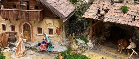 Eine detaillierte Miniaturkrippe zeigt eine ländliche Umgebung mit einem Haus, einer Scheune und verschiedenen Figuren, einschließlich Hirten, Tieren und einem Stern darüber.