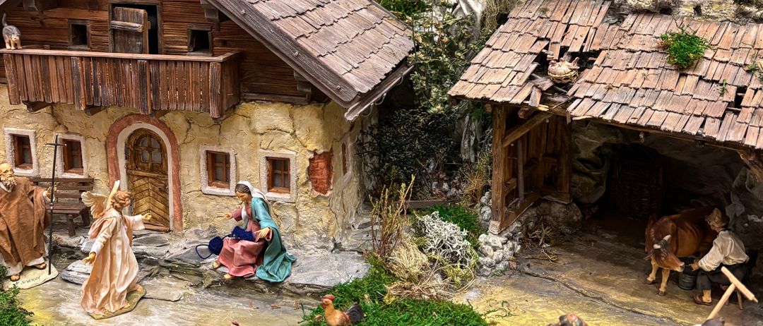 Eine detaillierte Miniaturkrippe zeigt eine ländliche Umgebung mit einem Haus, einer Scheune und verschiedenen Figuren, einschließlich Hirten, Tieren und einem Stern darüber.